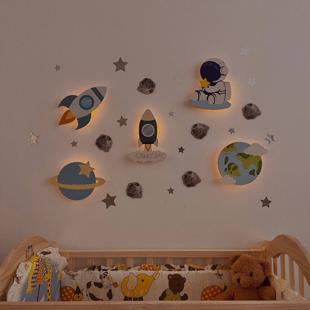 Personalized wooden wall light set for baby's room featuring rockets, planets, and stars, creating a cozy nighttime atmosphere.