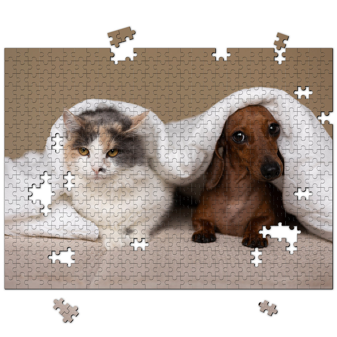 Custom pet photo jigsaw puzzle featuring a cat and dog snuggled under a blanket, pieces scattered around.