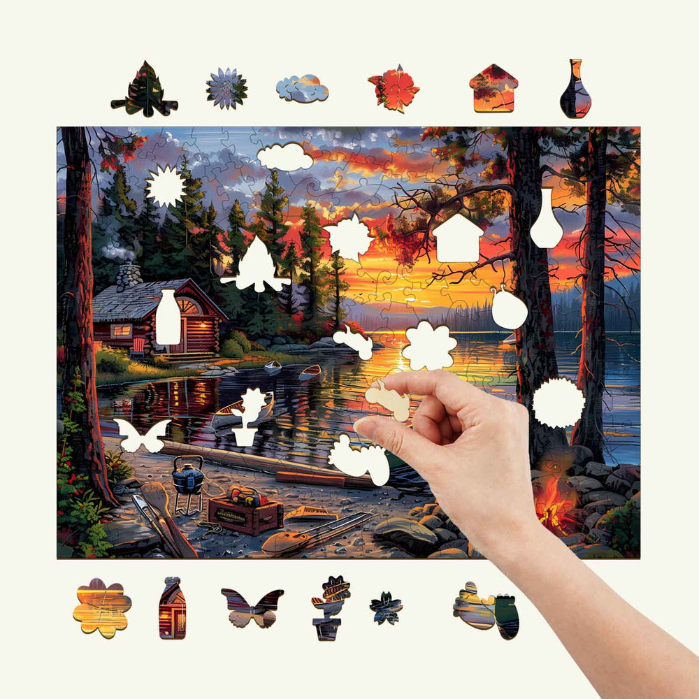 Hand placing a piece of the Canoe Lake-1 wooden jigsaw puzzle featuring a serene lakeside sunset scene.