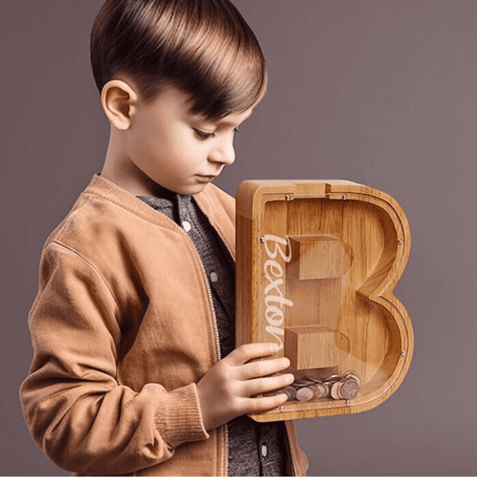 Child holding a personalized wooden letter piggy bank, promoting financial awareness and savings.